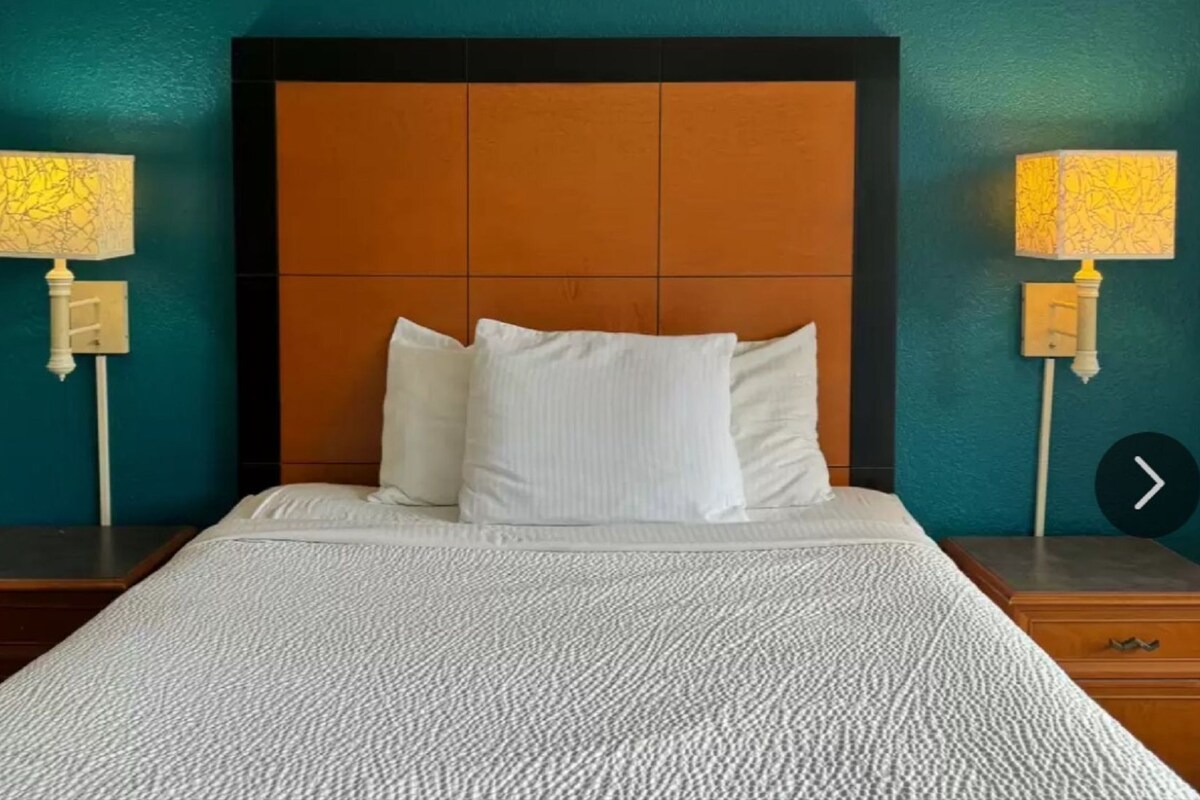 Una cama bien tendida con sábanas blancas, un cabecero de madera y dos lámparas de noche con pantallas estampadas.