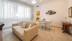 Un salon avec un canapé beige, une table à manger avec des chaises, un lustre et un mur décoré d’assiettes.