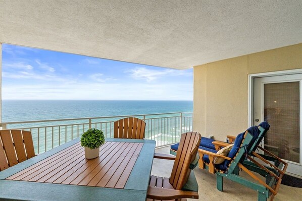 A balcony with a wooden table, chairs, and a potted plant.