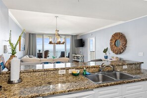 A modern kitchen with granite countertops, a built-in sink, and a dining area with a sofa and a television.
