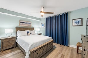 A bedroom with a bed, nightstands, a ceiling fan, and a large window with curtains.