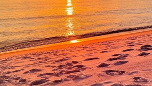 Una spiaggia con impronte che conducono verso l'acqua, un tramonto sullo sfondo e un cielo sereno.