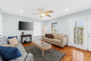 A living room with a sofa, coffee table, TV, and a ceiling fan.