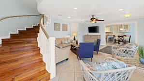 A spacious living area with a wooden staircase, a sofa, a blue armchair, and wicker furniture. - Sleeps 14, Game Room, Gated Beach Access, Pet Friendly (Panama City Beach)