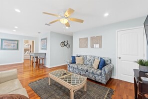 Un salon avec un canapé à motifs, une table basse, un ventilateur de plafond et une porte.