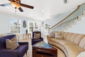 A spacious living room with a ceiling fan, a staircase, and a large window.