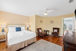 Une chambre à coucher avec un lit, deux chaises, une petite table, un ventilateur de plafond et une vue sur l’extérieur.
