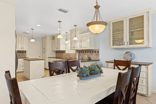 A spacious kitchen with white cabinetry, a central island, pendant lighting, and a dining area with a table and chairs.