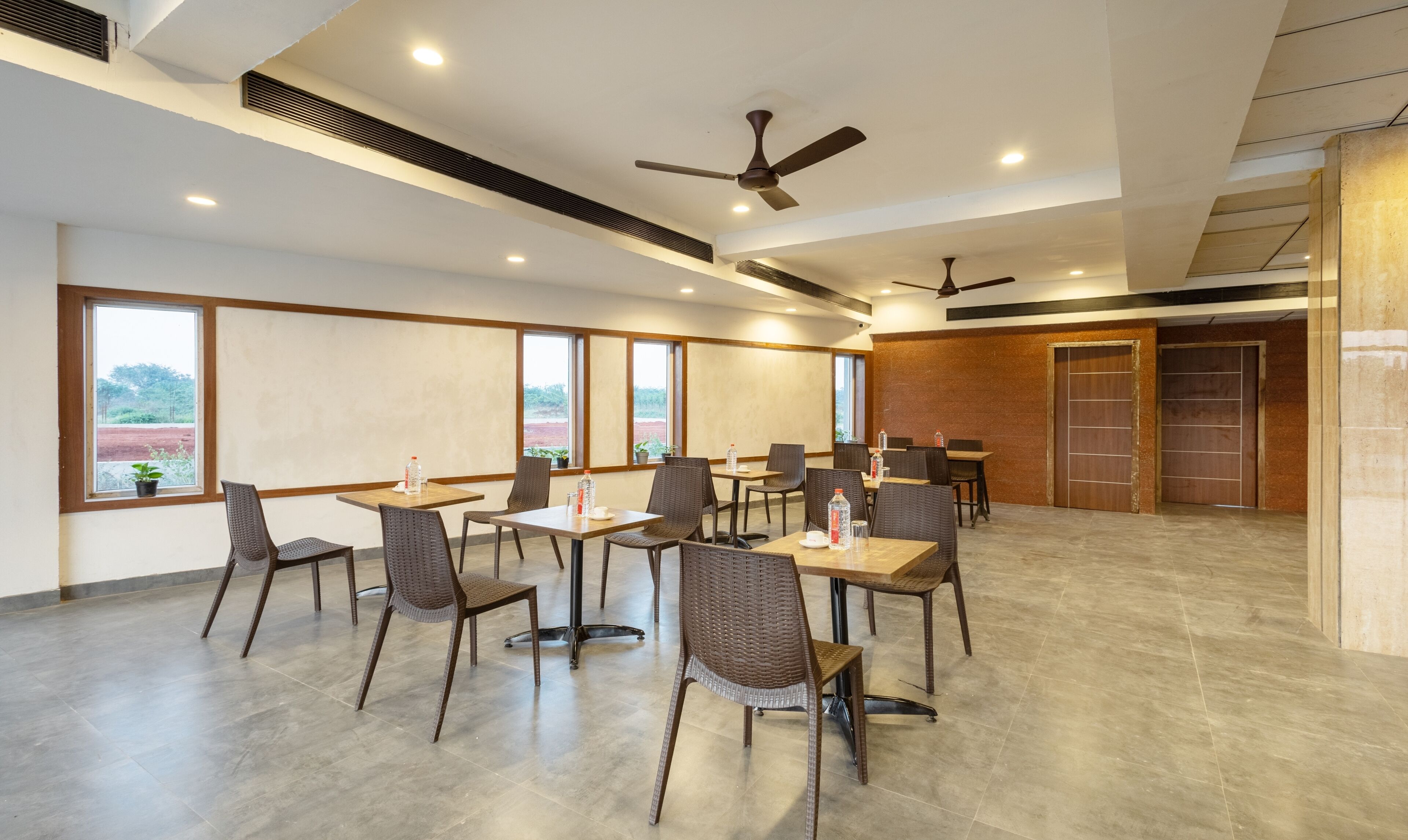 A spacious indoor dining area with high ceilings, multiple tables and chairs, and large windows offering views of the outdoors.