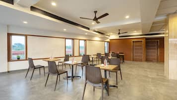 A spacious indoor dining area with high ceilings, multiple tables and chairs, and large windows offering views of the outdoors.