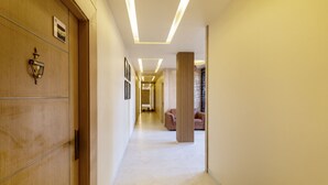 A modern hotel corridor with wooden paneling, a marble floor, and a central column.