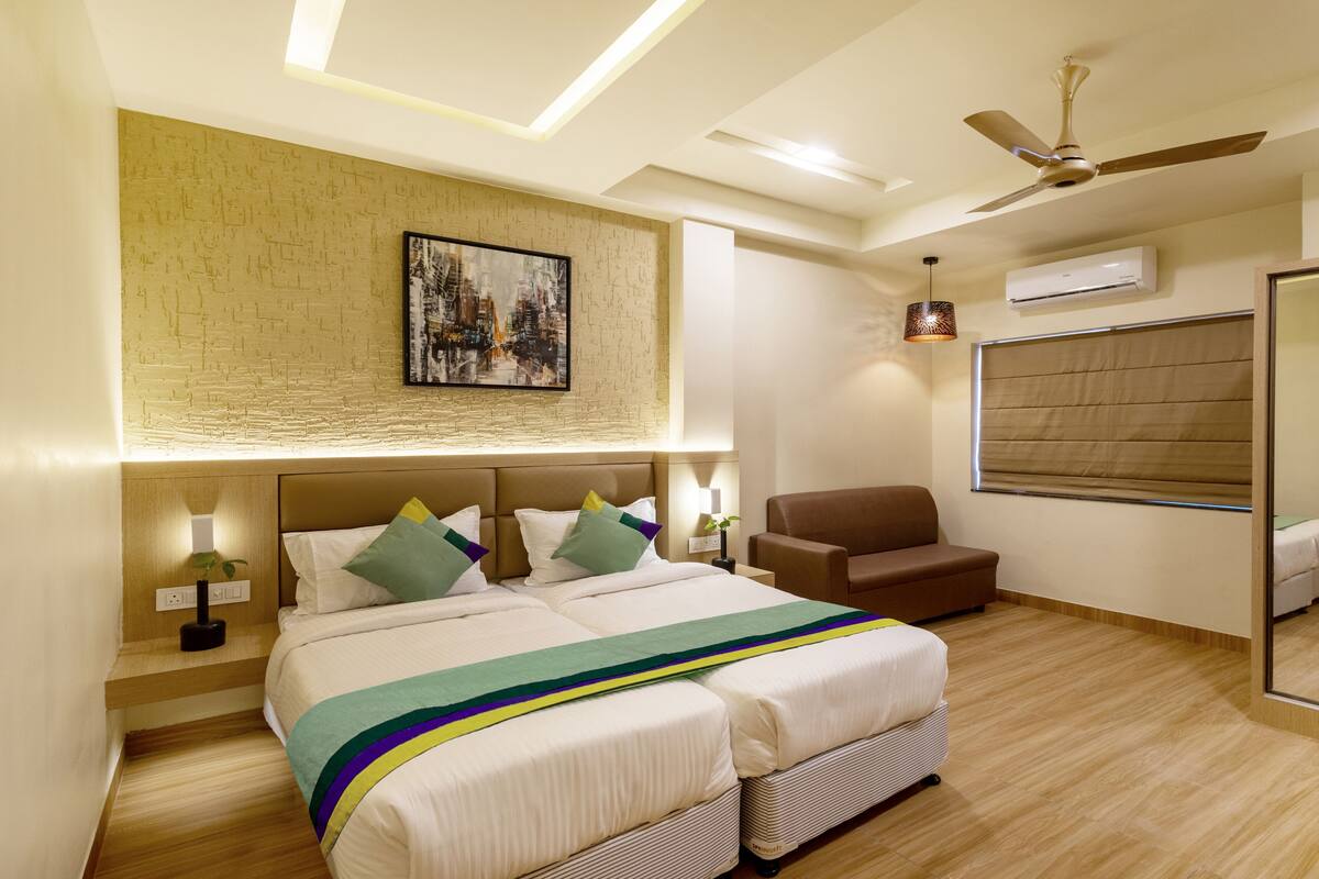 Ein modernes Hotelzimmer mit einem großen Bett, einem Sessel, einem Nachttisch, einer Lampe, einem Deckenventilator und einem großen Spiegel.
