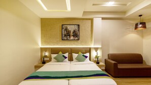 A hotel room with a large bed, two bedside tables with lamps, a brown armchair, and a cityscape painting on the wall.