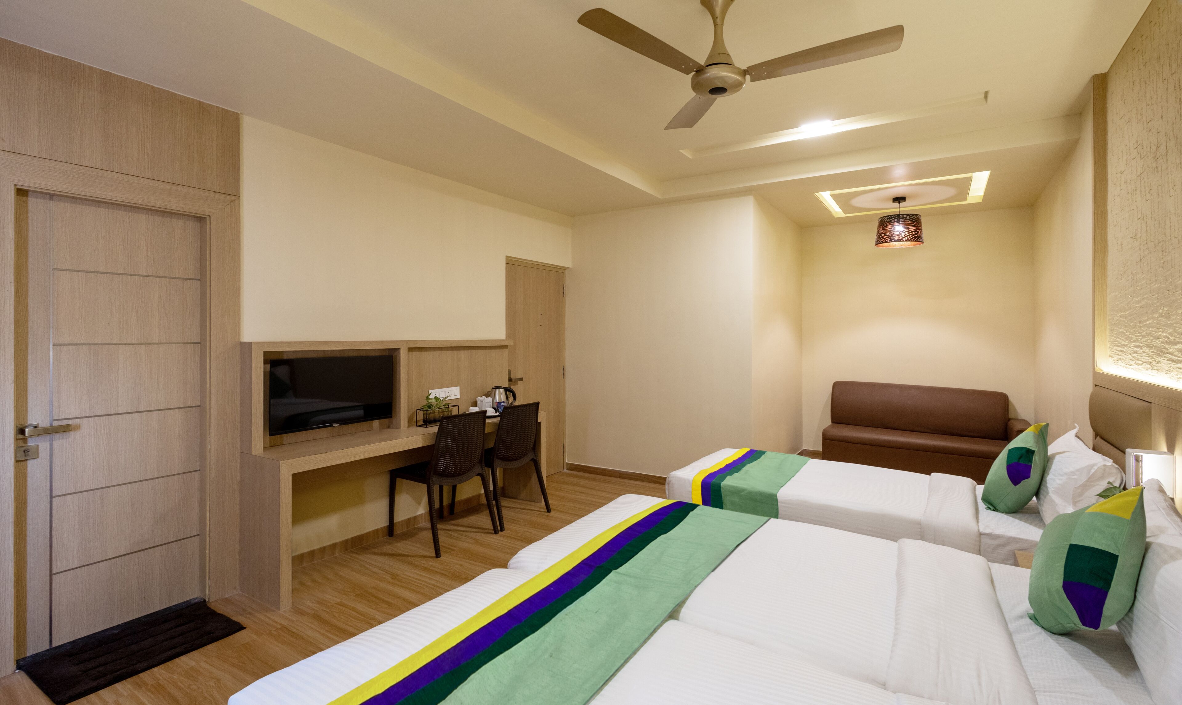 A hotel room with two beds, a desk with a TV, a ceiling fan, and a small table with a plant.