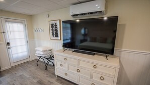 Una habitación con un aparador blanco, un televisor de pantalla plana montado encima y una puerta con ventanal.