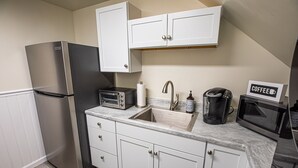 Una cocina con armarios blancos, un refrigerador de acero inoxidable, un tostador, un lavamanos, una cafetera y un microondas.