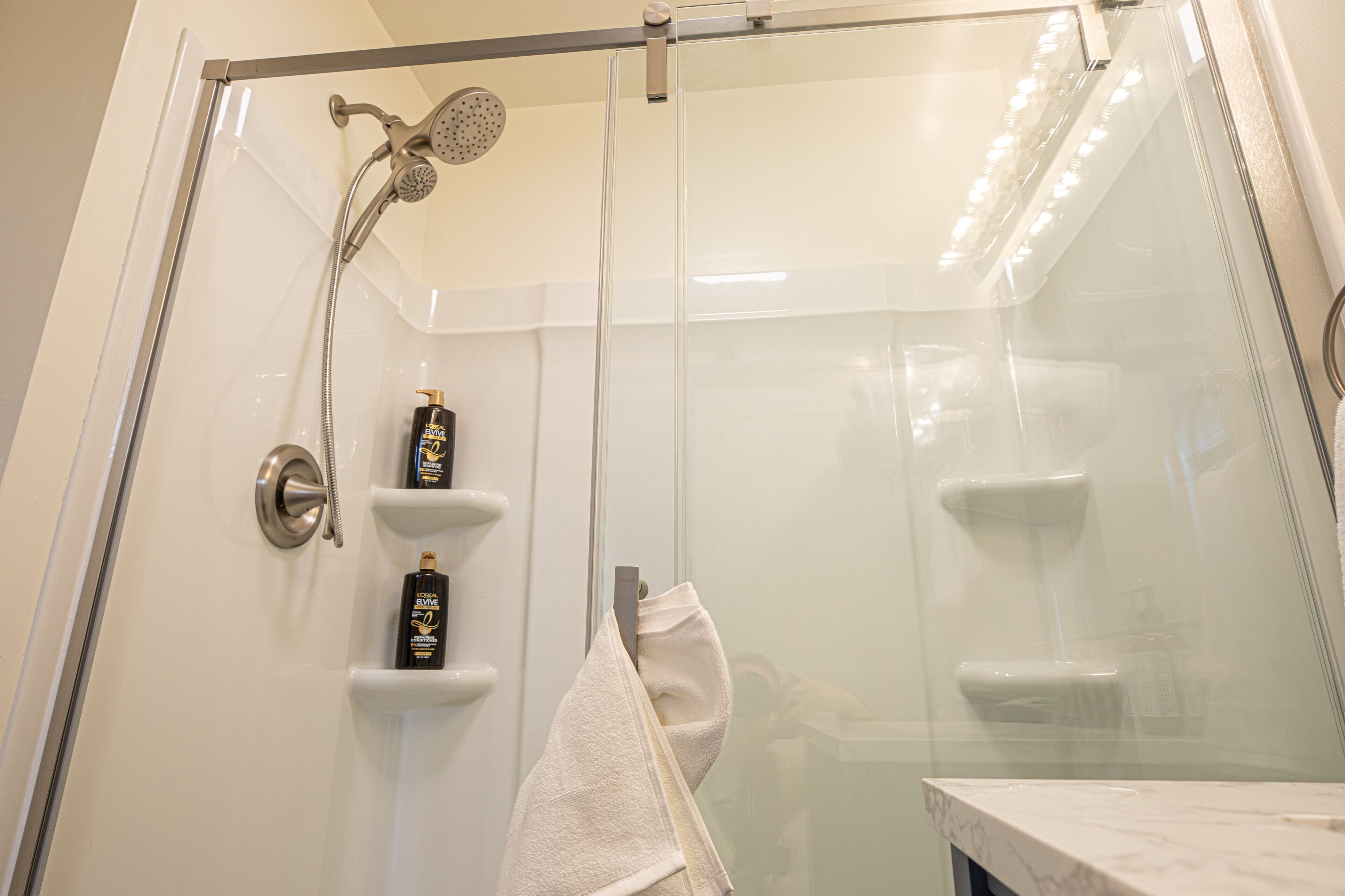 A glass-enclosed shower with a handheld showerhead and a wall-mounted faucet.