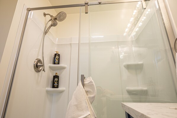 A glass-enclosed shower with a handheld showerhead and a wall-mounted faucet.