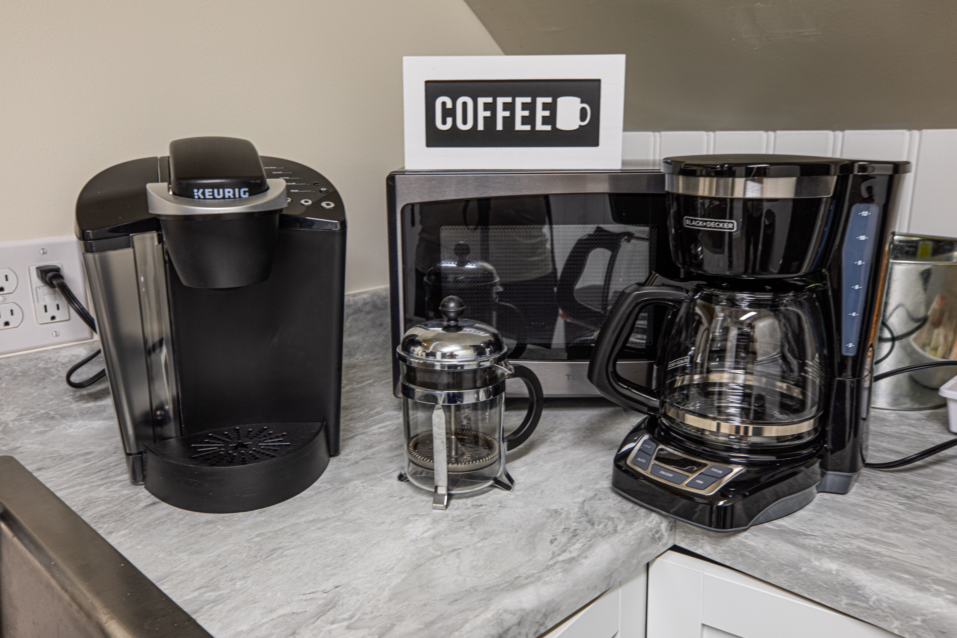 Une machine à café, une cafetière et un panneau indiquant « CAFÉ » sur un plan de travail de cuisine.