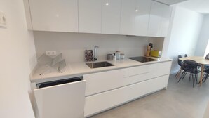 Eine moderne Küche mit weißen Schränken, einem eingebauten Geschirrspüler, einer Spüle und einem Essbereich mit Tisch und Stühlen.