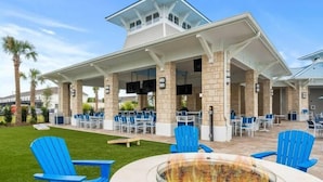 Un espace extérieur aménagé en terrasse, avec des fauteuils Adirondack bleus, un foyer et un coin salon couvert avec des tables et des chaises.