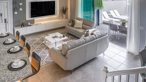 Un salon moderne comprenant un canapé, une table basse, un téléviseur et un coin repas avec des chaises et une table.