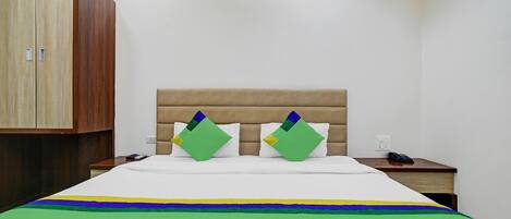 A hotel room with a bed, a wooden wardrobe, and a nightstand with a phone.