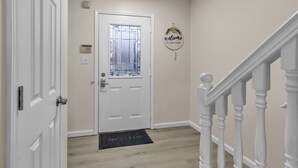 A hallway with a white door, a welcome sign, a doormat, and a staircase with white balusters. - Central Downtown Living (Buffalo)