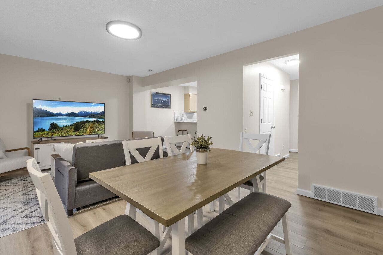Un salon moderne avec une table à manger en bois, des canapés gris et un t éléviseur à écran plat qui diffuse un paysage pittoresque.
