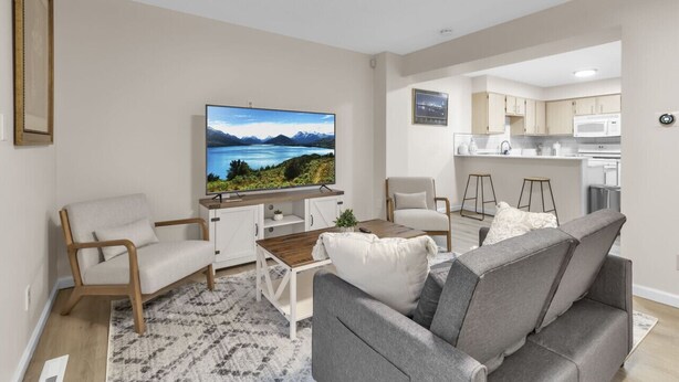 A modern living room with a flat-screen TV, grey sofas, a wooden coffee table, and a kitchen area in the background. - Central Downtown Living (Buffalo)