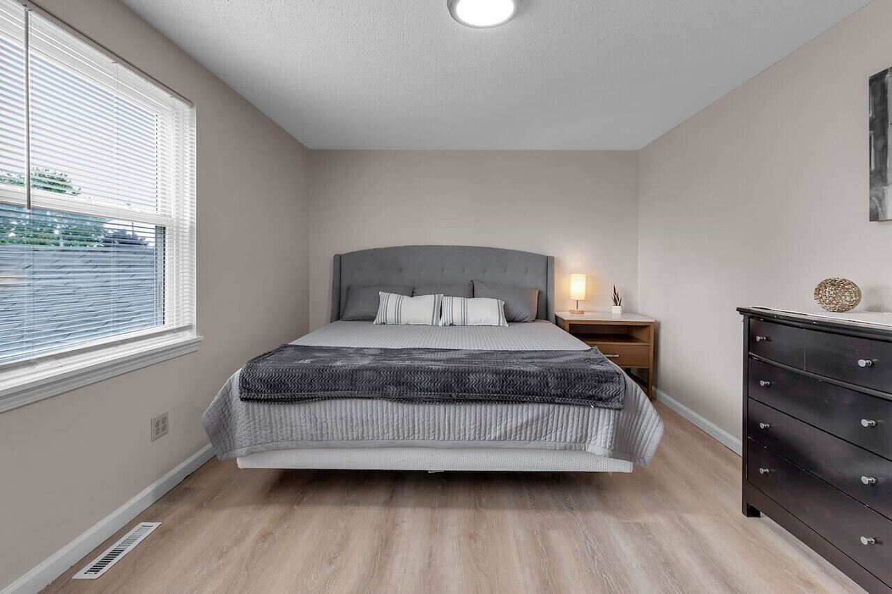 A bedroom with a bed, a nightstand, a dresser, and a window with blinds.