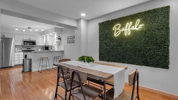 A modern kitchen with white cabinets, stainless steel appliances, and a dining area with a wooden table and chairs. - Living Large Downtown (Buffalo)