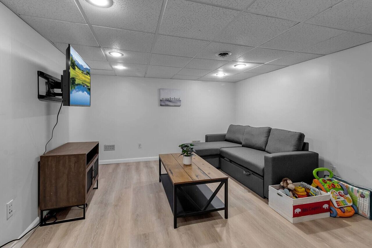 A modern living room with a grey sofa, a wooden coffee table, a TV mounted on the wall, and a small plant on the table.