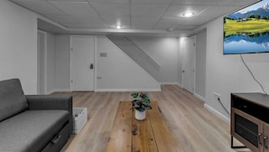 A modern living room with a grey sofa, a wooden coffee table with a plant, a flat-screen TV, and a staircase leading to another room. - Living Large Downtown (Buffalo)