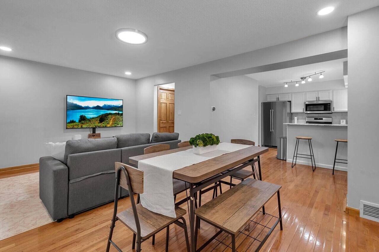 Ein modernes Wohnzimmer mit einem grauen Sofa, einem Holzesstisch und einem Fernseher an der Wand.