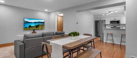 Ein modernes Wohnzimmer mit einem grauen Sofa, einem Holzesstisch und einem Fernseher an der Wand.