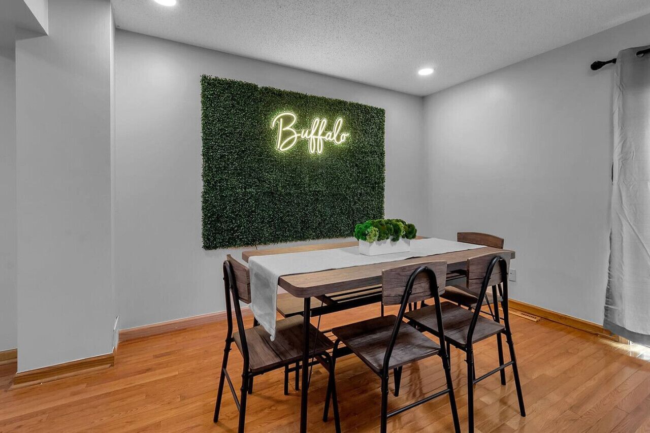 A dining area with a table and chairs, a neon sign on the wall, and a green wall.