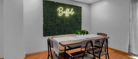 A dining area with a table and chairs, a neon sign on the wall, and a green wall.