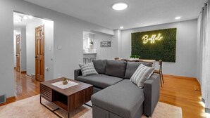 A modern living room with a sectional sofa, a wooden coffee table, and a neon sign on the wall. - Living Large Downtown (Buffalo)
