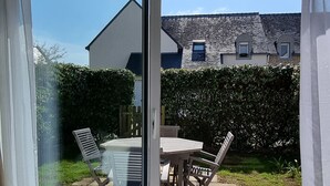 Habitació amb una porta corredissa de vidre que dona a un pati exterior. El pati té un paviment de rajoles i una taula amb cadires.