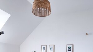 Un dormitori amb sostre inclinat, un llit amb colcha blava estampada, un capçal de llit de fusta i una làmpada penjant de fibra.