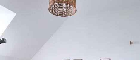 A bedroom with a sloped ceiling, a bed with a blue patterned bedspread, a wooden headboard, and a woven pendant light.