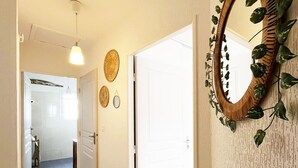 Un passadís amb terra de fusta, una panxa de vímet, un mirall amb una planta i una porta que dona a una altra habitació.