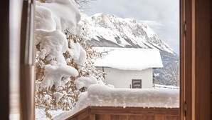 A wooden gate leading to a small white building with a snow-covered roof, set against a backdrop of snow-covered mountains.
