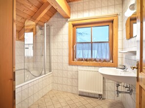 Une salle de bain avec une douche, une fenêtre avec des rideaux, un lavabo et un radiateur.
