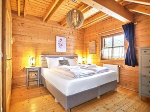 Une chambre dans une cabane en bois, avec un lit, des lampes de chevet, une fenêtre avec des rideaux et un radiateur.