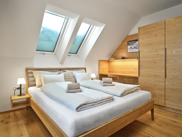 A modern bedroom with a large bed, skylights, wooden wardrobe, and a desk.