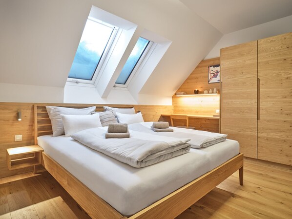 Un dormitorio moderno con techo inclinado, tragaluces, estructura de cama de madera y armario empotrado de madera.