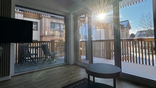 En moderne stue med et rundt bord, et fladskærms-TV og en stor skydedør, der fører ud til en terrasse.