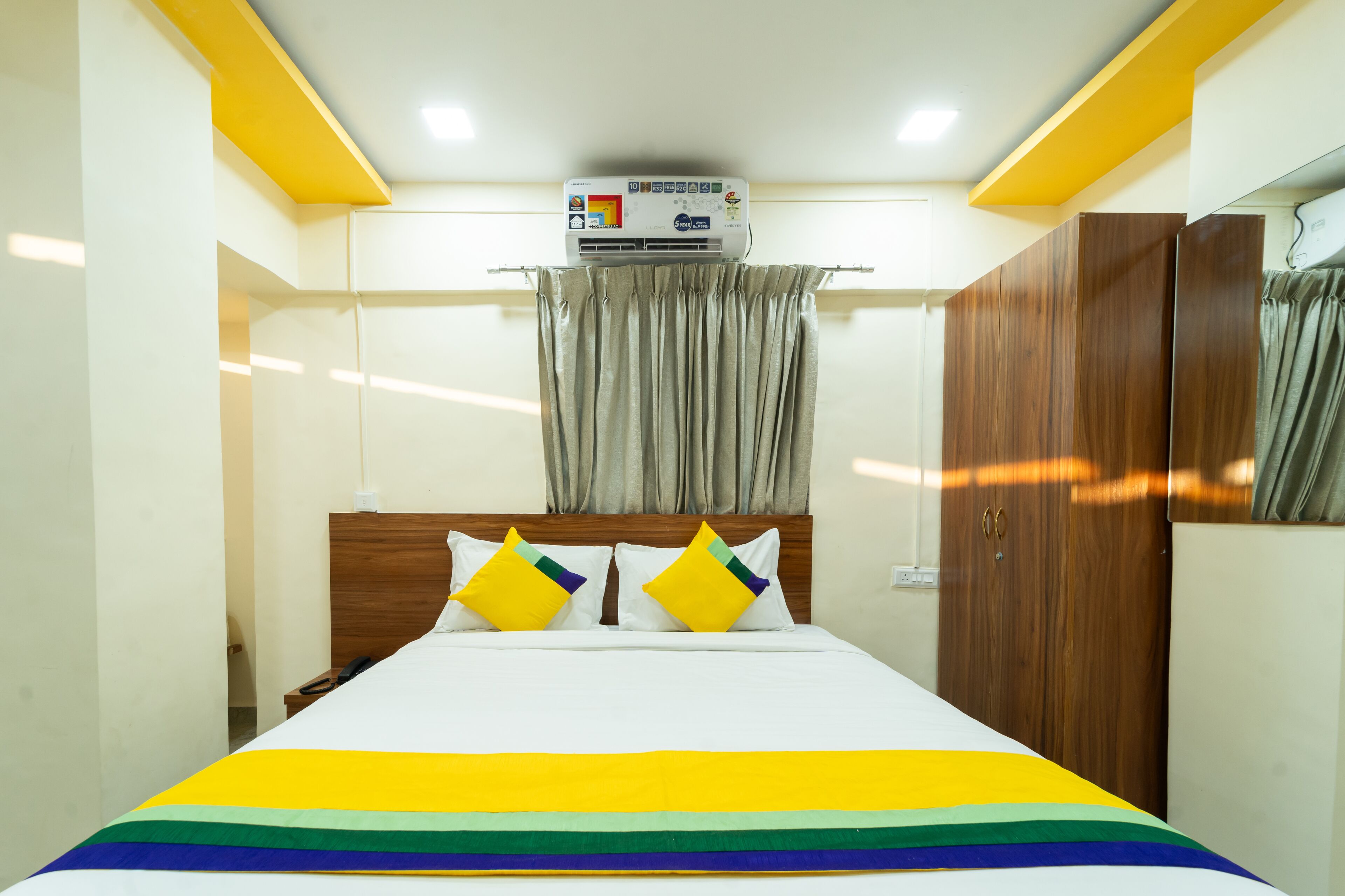 Una camera d'albergo con un letto, tende, un armadio in legno e un condizionatore d'aria.